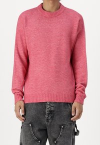 Pink knitted sweater with a crew neckline and ribbed cuffs and hem, paired with gray jeans featuring side pockets and a textured finish.