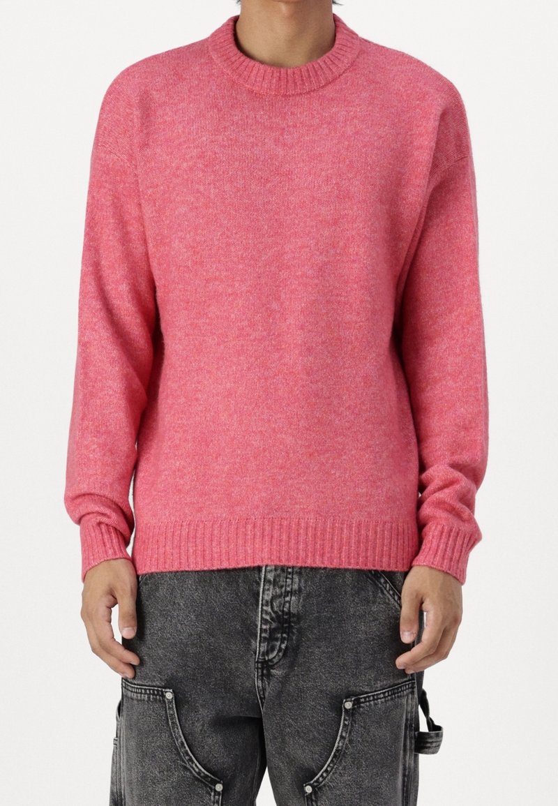 Pink knitted sweater with a crew neckline and ribbed cuffs and hem, paired with gray jeans featuring side pockets and a textured finish.