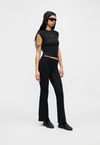 Μαύρο ριμπ crop top με κοντά μανίκια, συνδυασμένο με μαύρο παντελόνι με φαρδιά μπατζάκια και μαύρα αθλητικά παπούτσια. Αξεσουάρ περιλαμβάνουν μαύρο καπέλο και γυαλιά ηλίου.