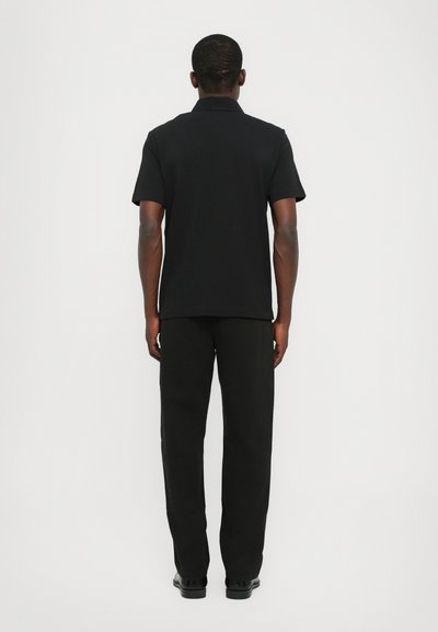 Polo shirt noir avec un col, des manches courtes et une coupe décontractée, associé à un pantalon noir et des chaussures sombres.