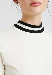 Vit skjorta med svart och vit randig ribbad krage. Mjuk textur, figursydd design och rund halsringning. Minimalistisk och ren estetik.