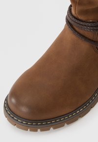 Bruine leren laars met een ronde neus, gestikte details en gevlochten leren accenten rond de enkel. Dikke rubberen zool met grip.