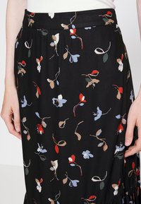 Saia preta com padrão floral, apresentando uma variedade de flores e folhas coloridas em vermelho, azul, bege e verde, com um acabamento godê e cintura elástica.