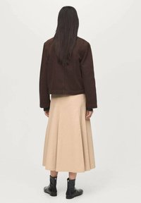 Veste courte marron, jupe évasée beige et bottines noires. Texture de tissu lisse, design simple et silhouette arrivant au genou.