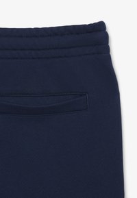 Felpa blu navy, realizzata in tessuto con vita a coste e una singola tasca posteriore con apertura orizzontale. Texture liscia, senza motivi.