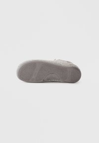 Semelle de chausson gris clair avec un caoutchouc texturé pour une bonne adhérence, un dessus en feutre doux et une semelle intérieure rembourrée pour le confort.