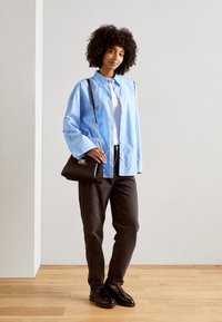 Světlomodrá košile na zapínání, pod ní bílý tričko, tmavé džíny, černá kabelka s řetízkovým popruhem a černé mokasíny. Kudrnatý účes.