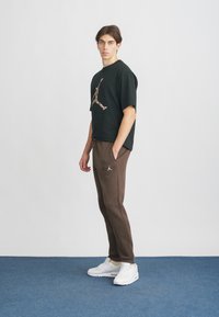 Czarny t-shirt z wielokolorowym logo Jordana, w zestawieniu z brązowymi spodniami dresowymi. Białe sneakersy dopełniają strój. Gładki materiał i luźny krój.