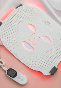 Masque facial LED blanc avec design perforé ; émet une douce lumière rouge. Inclut une télécommande grise avec un écran et trois boutons.