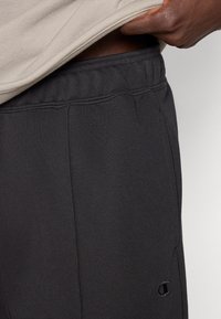 Μαύρο παντελόνι φόρμας από απαλό ύφασμα, με ελαστική μέση και λεπτομέρειες με ραφή στο πλάι. Ένα μικρό λογότυπο είναι ορατό στο πόδι.