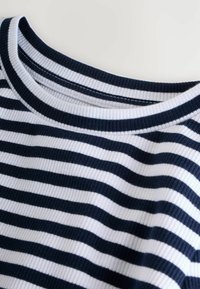 Chemise à rayures navy et blanches à manches longues avec une texture côtelée, présentant un large col rond et des détails en tissu contrastants au niveau du col.