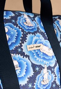 Zila, rakstu bagāža ar Moomin varoņiem tumši zilā fona, ar stingriem jūras zilas krāsas rokturiem un auduma etiķeti.