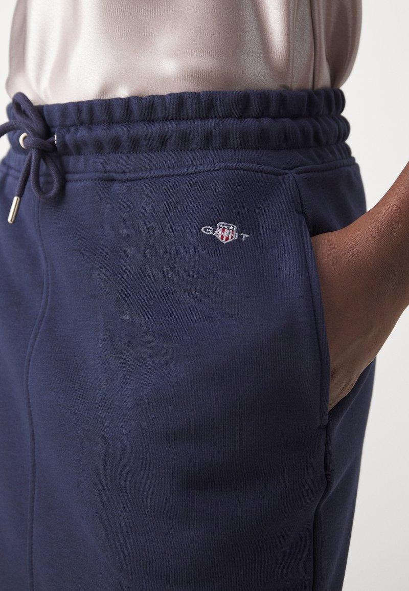 Granatowe dresy wykonane z miękkiej tkaniny, z elastycznym pasem ze sznurkiem i bocznymi kieszeniami. Zawierają małe logo na udzie.