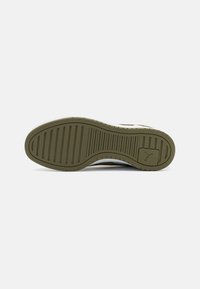 Sole of a sneaker featuring a textured green rubber material with horizontal and vertical grooves, a white edge, and a logo detail.