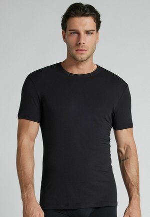 Mand med kort mørkt hår iført en tætsiddende ensfarvet sort kortærmet T-shirt, stående mod en grå baggrund.