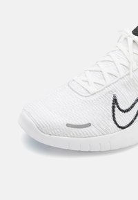 White athletic shoe with a textured mesh upper, black logo accent, and a white rubber sole. Features a lace-up design.