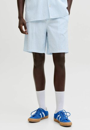 Čovjek nosi svijetloplave i bijele prugaste šortse, bijele čarape i svijetloplave tenisice s bijelim prugama i gumenim đonovima.