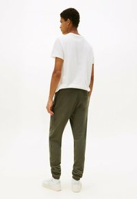 Witte T-shirt, khaki sweathose, elastische manchetten, zijzakken, voorzien van een klein logopatch, gecombineerd met witte sneakers.