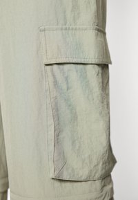 Ανοιχτοπράσινες βερμούδες cargo με υφή, διαθέτοντας πλαινές τσέπες και αντίθετο ράψιμο. Τα υλικά φαίνονται ελαφριά και ανθεκτικά.