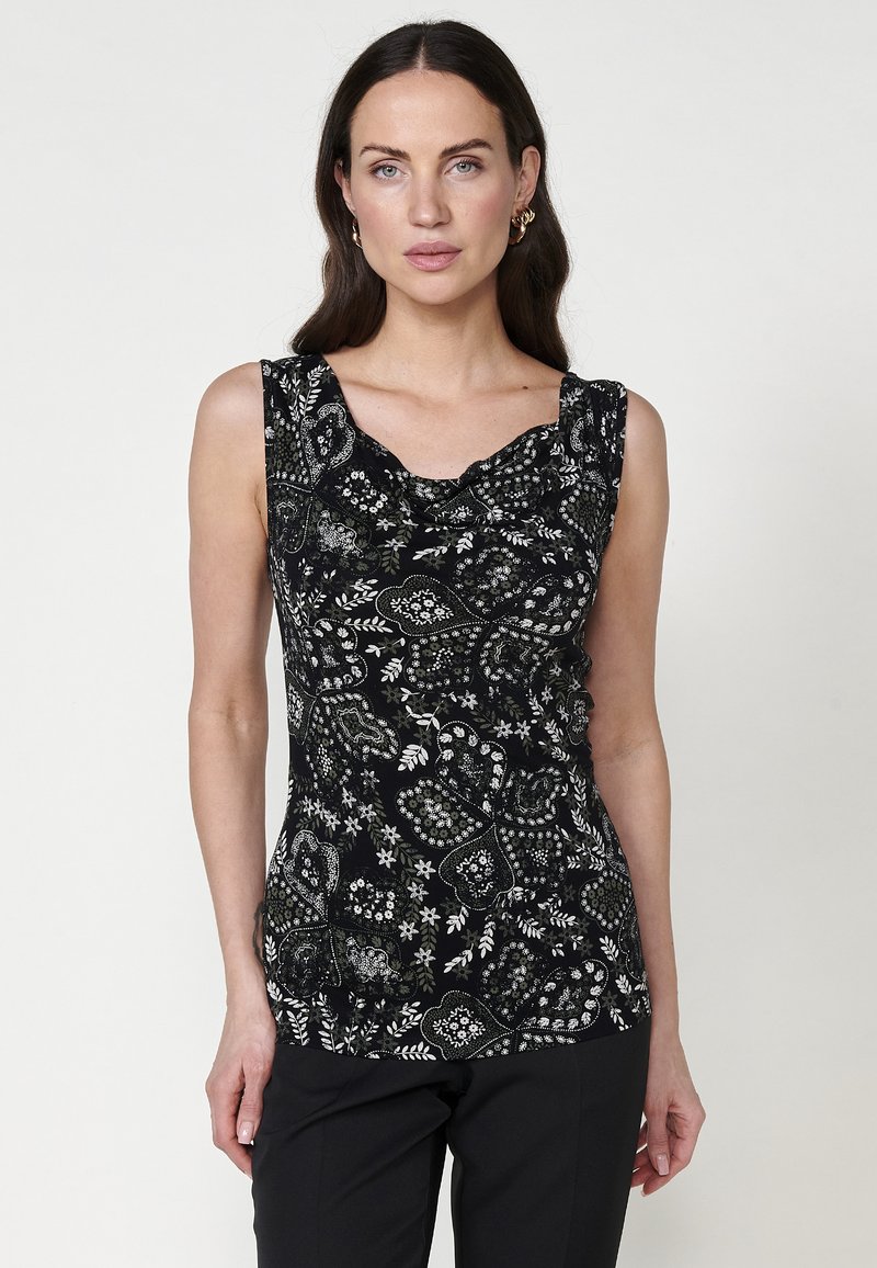 Haut sans manches noir avec un col drapé, présentant des motifs floraux et paisley blancs complexes, ainsi qu'un tissu texturé.