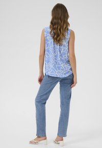 Haut sans manches bleu clair avec un motif abstrait blanc, associé à un jean droit bleu clair et des sandales à talons blancs.