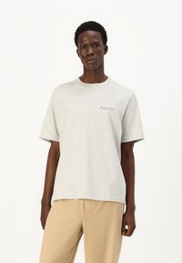 Tricou gri cu mânecă scurtă, dintr-un material ușor, având un gât rotund și un detaliu de text mic pe zona stângă a pieptului.