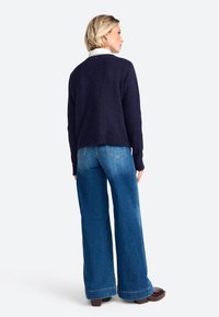 Maglione in misto lana blu navy con vestibilità rilassata, maniche ampie e fondo a costine, abbinato a jeans in denim azzurro chiaro a zampa d'elefante e scarpe con plateau marroni.