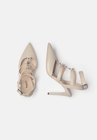 Scarpe con tacco alto beige con punta appuntita, fasce sovrapposte e dettagli in argento. Realizzate in pelle liscia con un design elegante.