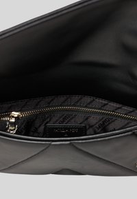 Interno di una borsa a tracolla in pelle nera con una tasca con zip, dettagli trapuntati e una fodera a fantasia con etichetta del marchio. Hardware in tonalità oro visibile.