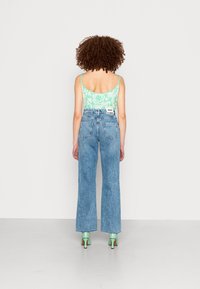 Top de tanque padrão verde menta, jeans de cintura alta azul claro com pernas largas, e saltos verdes brilhantes, com um penteado natural com cabelo encaracolado.