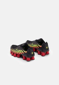 Mustat ja keltaiset gradientti Nike lenkkarit, joissa on pehmustetut kieliosat, tekstuuripinnat ja punaiset vaimennetu pohjat, joissa on erottuvat spiraalikorostukset.