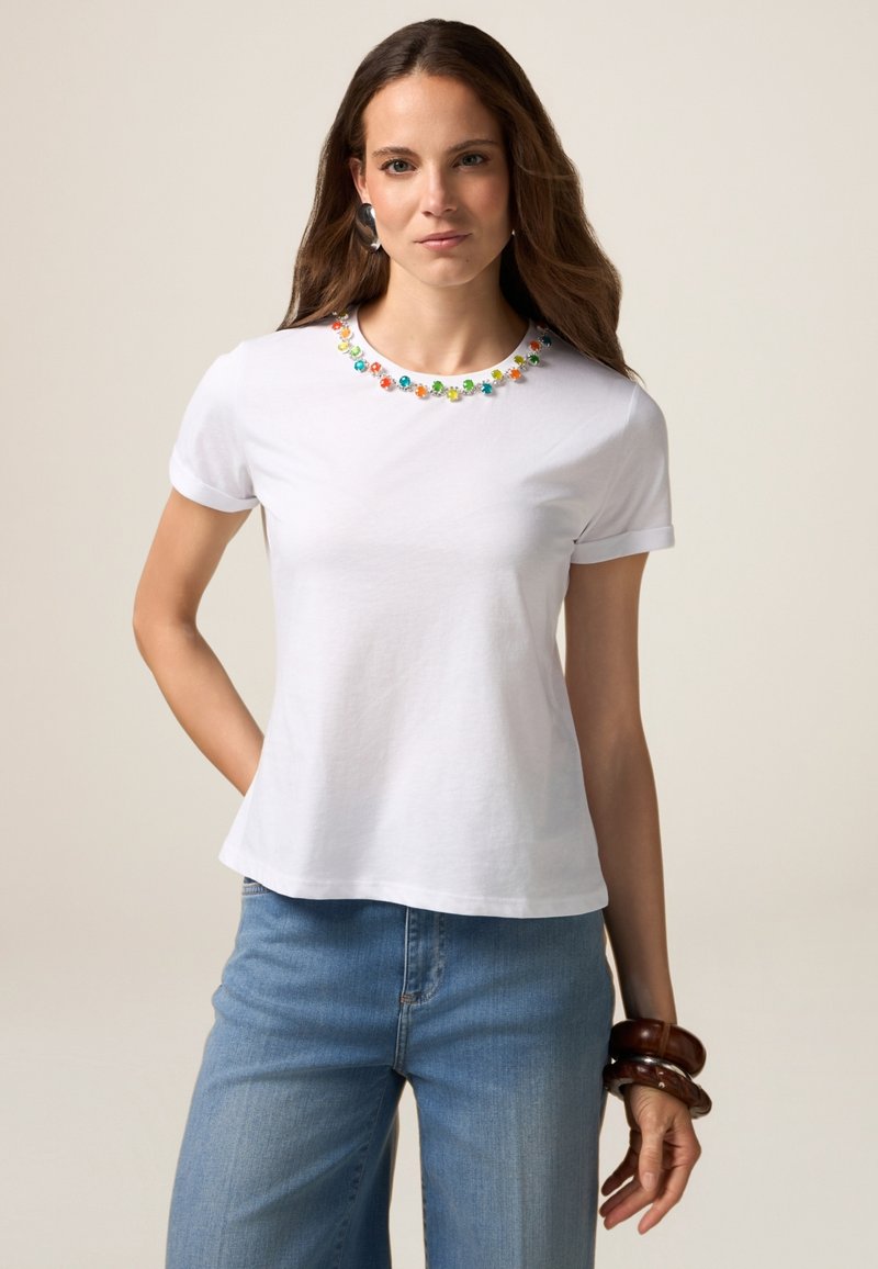 Hvid kortærmet t-shirt med en rund halsudskæring prydet med farverige blomsterdekorationer. Kombineret med lyseblå denim.