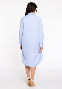 Blau-weiß gestreiftes Hemdkleid mit Kragen, langen Ärmeln und abgerundetem Saum, kombiniert mit weißen Wedge-Sandalen. Glatte Stofftextur.