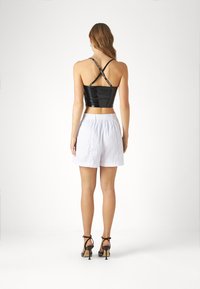 Top court en verni noir avec des bretelles croisées, associé à un short blanc à taille élastique. Des talons aiguilles complètent l'ensemble.