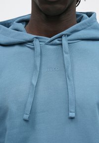 Lichtblauwe hoodie van zachte stof, met een geribbelde capuchon, trekkoorden en een reliëflogo aan de voorkant.