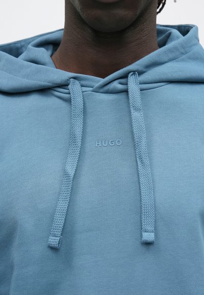 Sweat à capuche bleu clair en tissu doux, avec une capuche côtelée, des cordons de serrage et un logo en relief sur le devant.