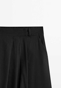 Pantalons plissés noirs avec une texture lisse, dotés d'une taille droite et de poches latérales, conçus pour une silhouette épurée.