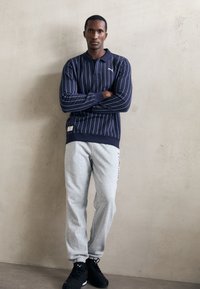 Marine stribet langærmet polo med krave, parret med grå sweatpants. Poloen har et lille logo og en blød tekstur. Sorte sportsko.