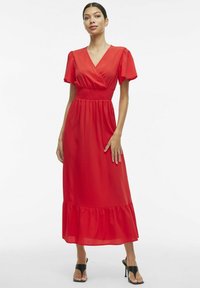 Červené šaty s krátkymi puff rukávmi, smúteným pásom a rozšíreným lemom. Vyrobené z ľahkého materiálu. Ozdobené jemnou textúrou.