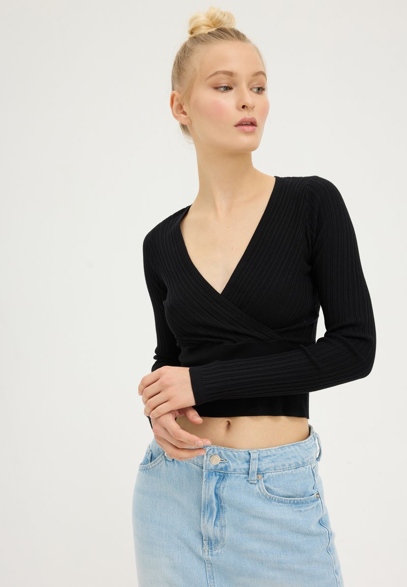Svart ribbet langermet innpakningsbluse med dyp V-hals, kombinert med lyseblå høyhånds denimskjørt.