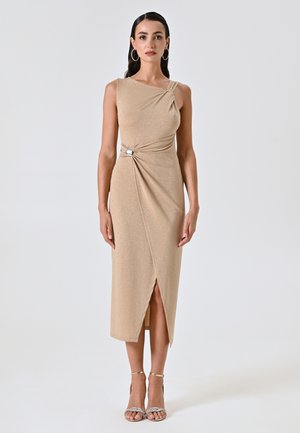 Beige, ärmelloses Kleid mit einem gedrehten Design in der Taille, das einen Schlitz in der Vorderseite und ein dekoratives Element aufweist. Glitzernde Textur steigert die visuelle Attraktivität.
