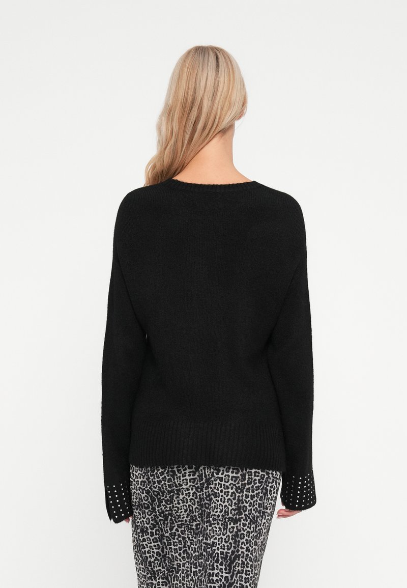 Maglione nero con maniche lunghe, bordo a costine e polsini decorati. Texture morbida. Abbinato a pantaloni con stampa leopardata.