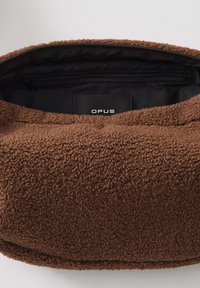 Borsa in pile marrone con una tasca interna zip nera e un'etichetta nera che legge "OPUS" all'interno.
