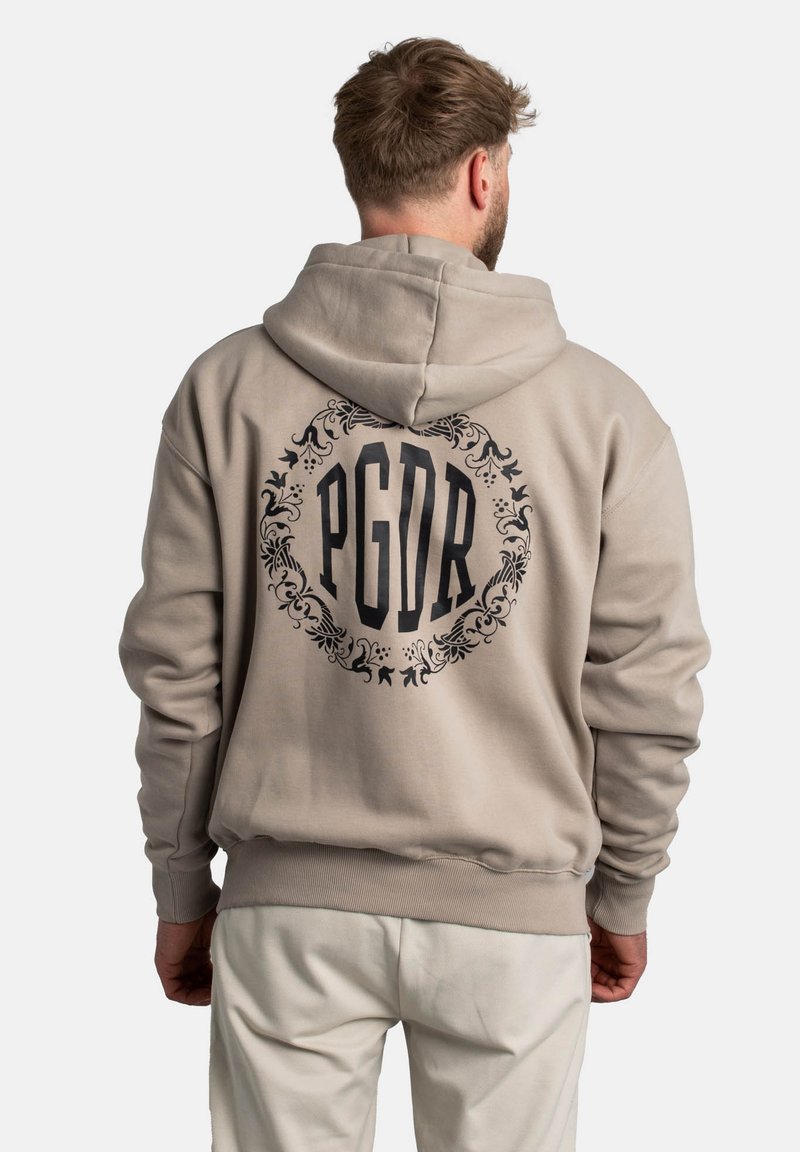 Sudadera beige con un gran gráfico negro de PGDR rodeado de un detallado ornamental en la parte posterior. Presenta una capucha con cordón y puños acanalados.
