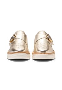 Metalliska guldiga slip-on skor med perforerat mönster, rund tå och vit, strukturerad sula. Har ett dekorativt band och en rund spänne.