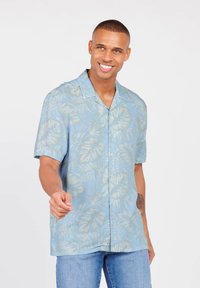 Helles blaues Kurzarmhemd mit einem tropischen Blattmuster in Creme, im Button-Down-Design und lässigem Schnitt, kombiniert mit blauen Jeans.