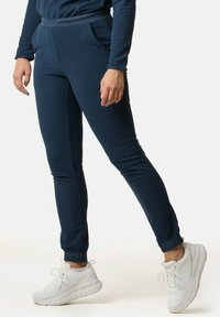 Marine joggers lavet af blødt stof med et tætsiddende design, der har sidelommer og ribbede manschetter, parret med hvide sportsko.