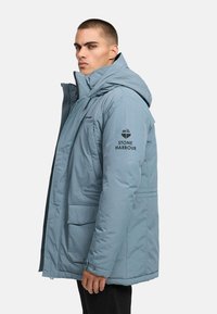 Smaržīgs zila parka jakas ar kapuci, divām priekšējām kabatām un melnu "STONE HARBOUR" logo uz piedurknes. Izgatavota no gludas, izturīgas auduma.