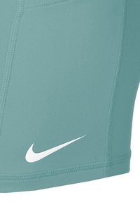 Nike sportske kratke hlače u svijetlo tirkiznoj boji, izrađene od glatkog materijala s prozračnom teksturom. Imaju bijeli logo i kontrastne šavove.