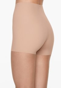 Naadloze, hoge shaping shorts van licht nude stof, met een gladde textuur en een aansluitend ontwerp, die tot halverwege de dij reikt.